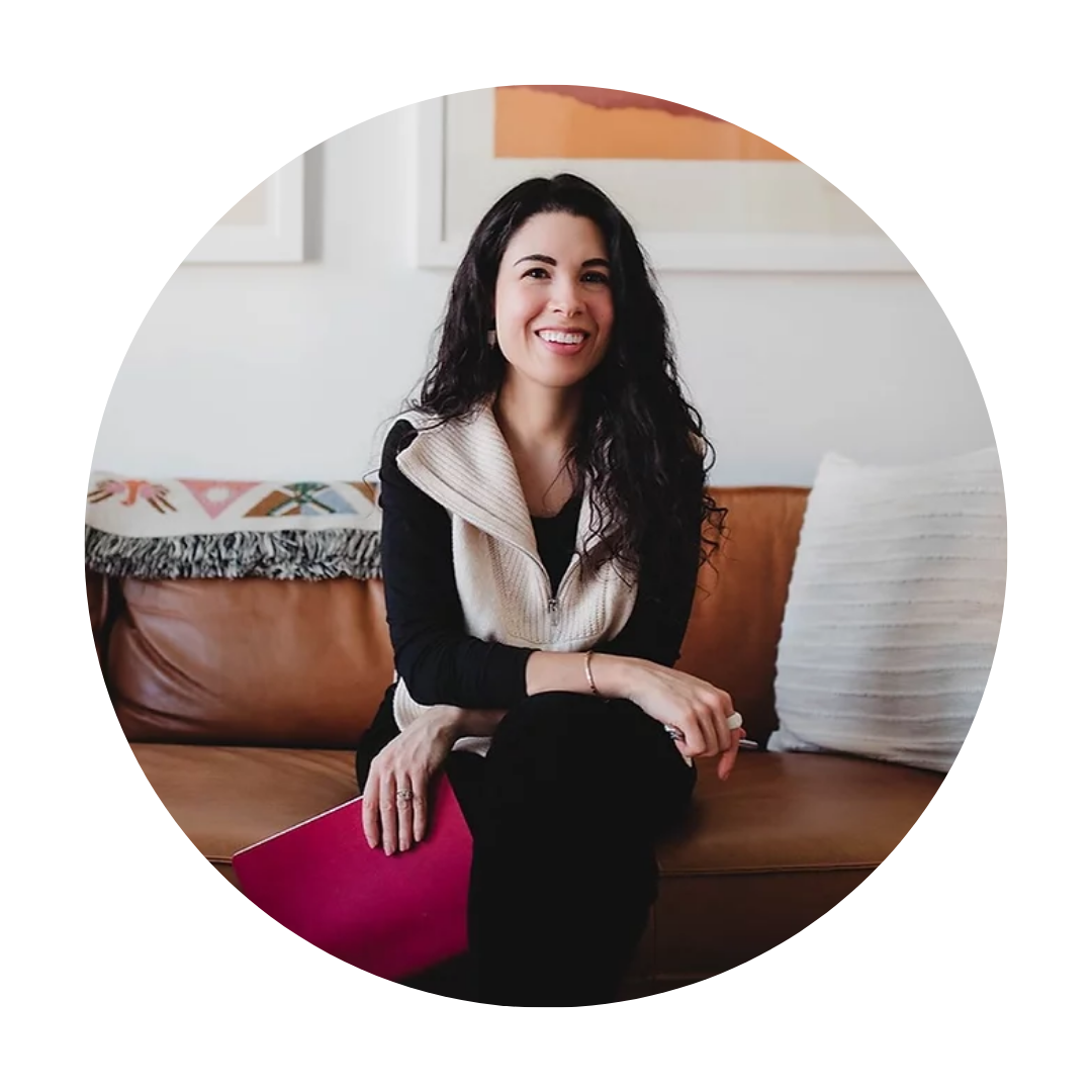Stephanie sitting on a brown leather couch looking slightly away from the camera holding a magenta notebook