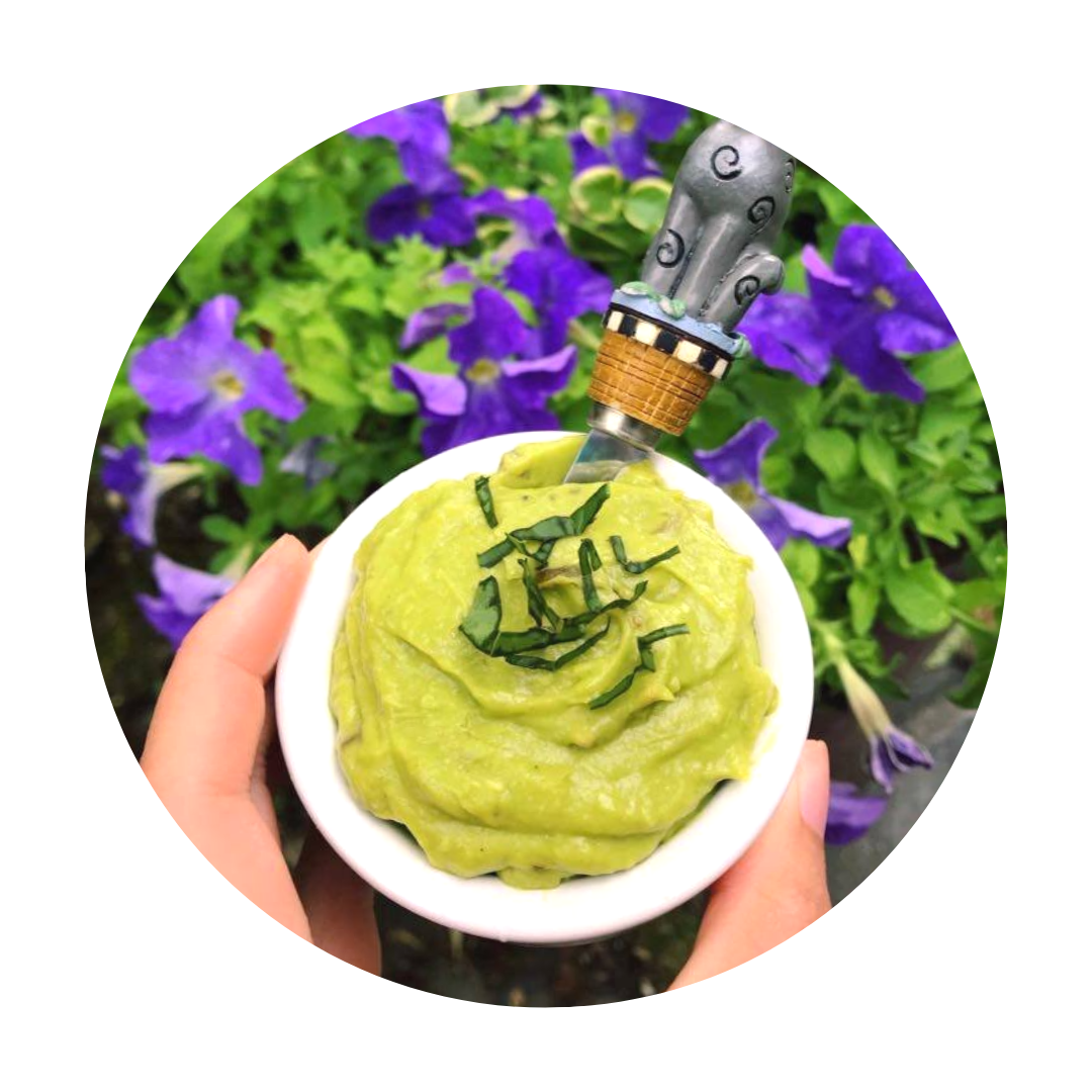 Avocado aioli in a small white ramekin held in front of a bed of violet flowers